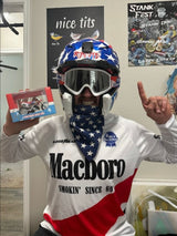 Person in motocross gear holding a Ronnie Mac bike replica, celebrating with a thumbs-up in a cool indoor setting.