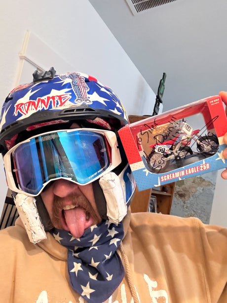 Fan showing off personalized signed Ronnie Mac Screamin Eagle bike replica in a helmet and goggles.