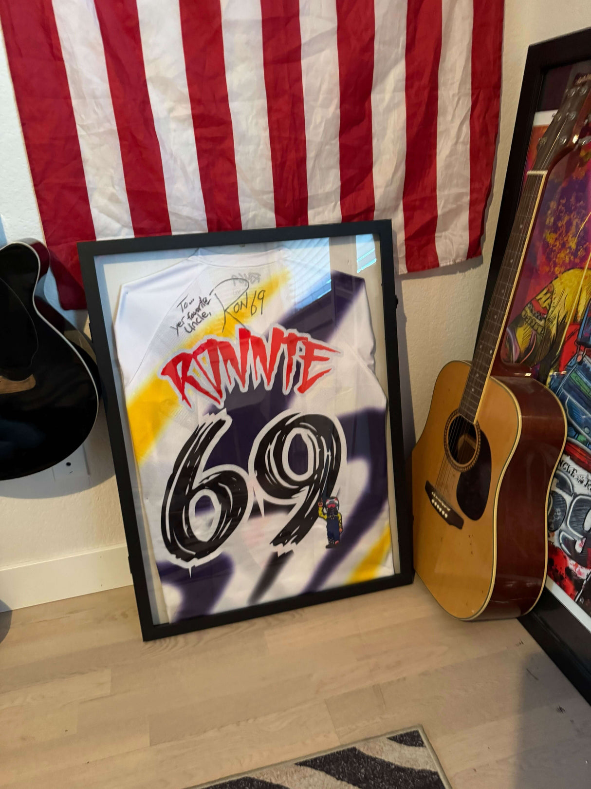 Ronnie Mac autographed limited edition jersey in a frame, displayed with American flag and guitars.