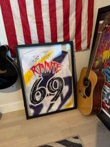 Ronnie Mac autographed limited edition jersey in a frame, displayed with American flag and guitars.