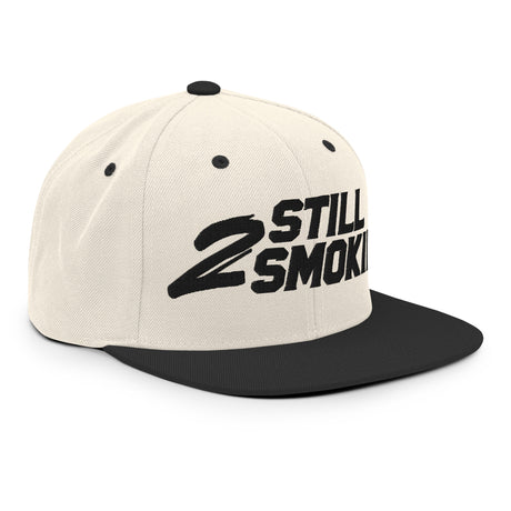 "2 Still Smoking embroidered snapback hat with flat brim and structured design featuring bold black lettering on cream fabric"